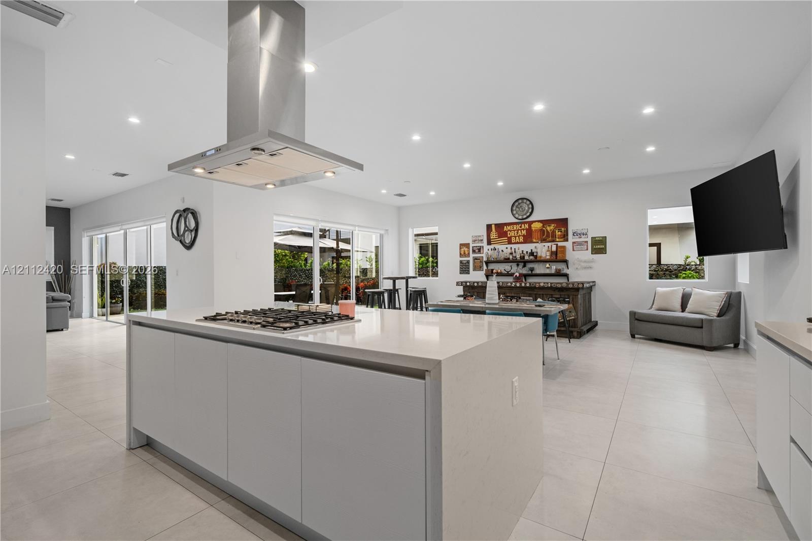 Kitchen featuring a large central island with quartz countertops, built-in gas cooktop, stainless steel ventilation hood, and light-colored tile flooring