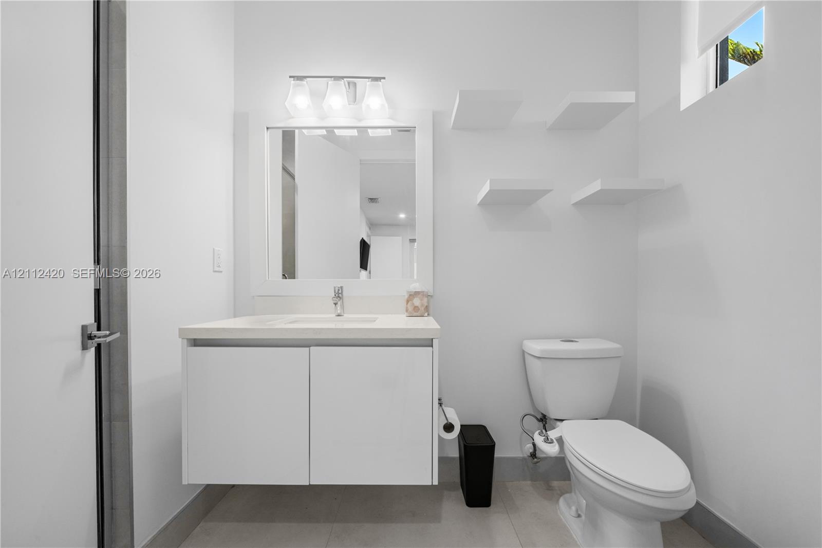 Modern floating vanity with a solid-surface countertop and integrated sink, complemented by built-in wall shelving, a rectangular mirror, and a three-light fixture