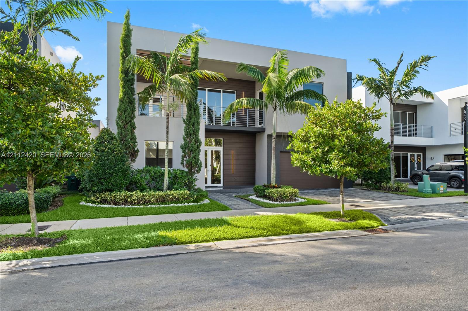 Modern two-story residence featuring a smooth stucco finish, horizontal wood-tone siding, a glass-railed upper balcony, and paver driveway Modern two-story residence featuring a smooth stucco finish, horizontal wood-tone siding, a glass-railed upper balcony, and paver driveway