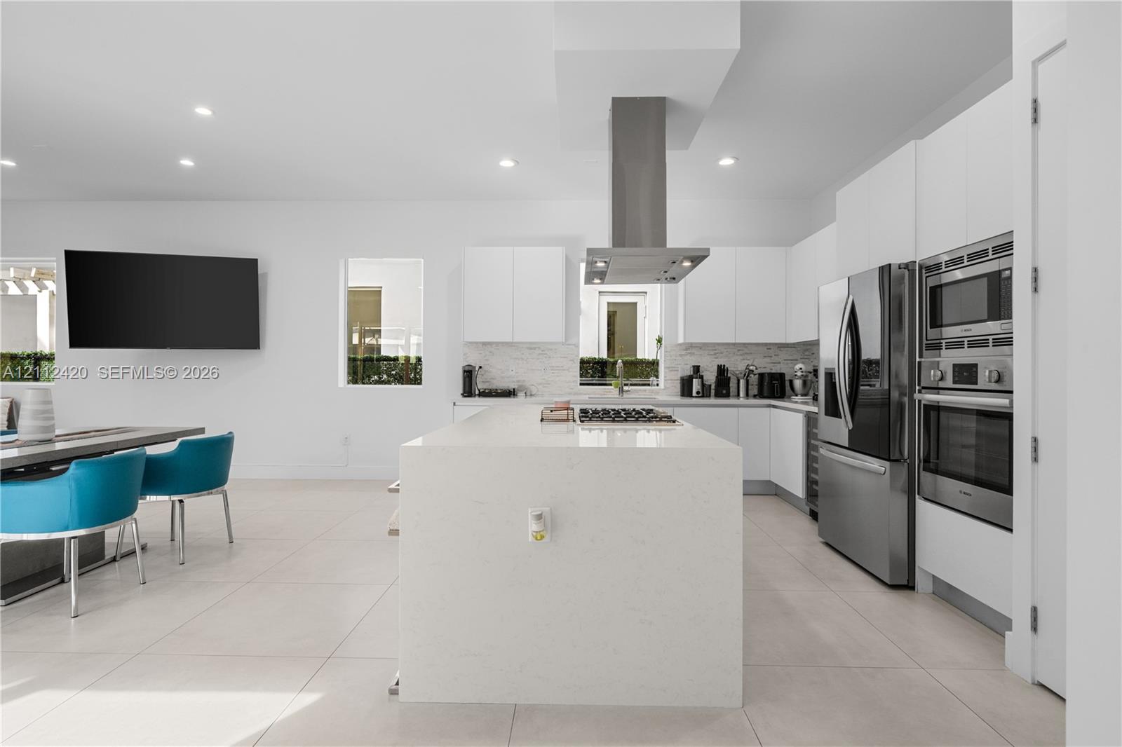 Kitchen featuring a central island with a solid surface countertop, stainless steel appliances, built-in double wall ovens, a stainless steel range hood, and flat-panel cabinetry