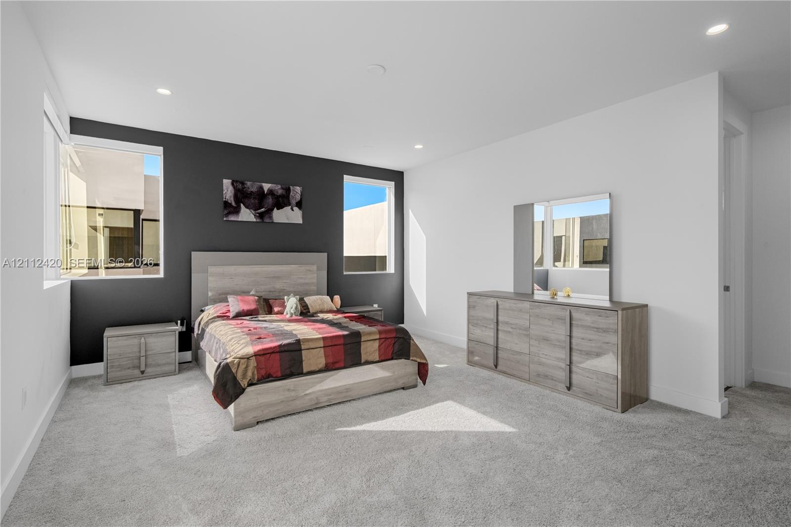 Neutral-toned carpeting, high-contrast dark accent wall, recessed lighting, and large windows providing natural illumination
