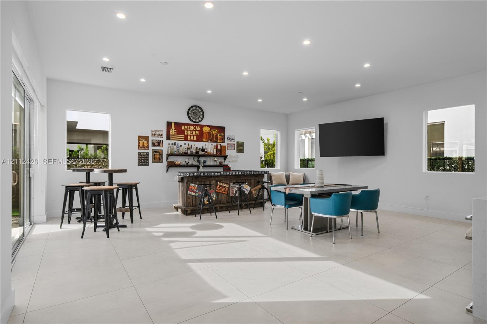 Spacious room featuring large-format tile flooring, recessed lighting, and a built-in bar area with wood cabinetry