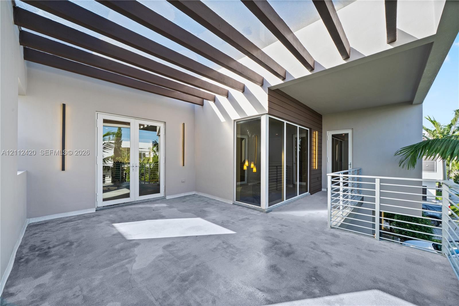 Covered terrace featuring a decorative pergola, concrete flooring, exterior wall-mounted lighting, and horizontal metal railings
