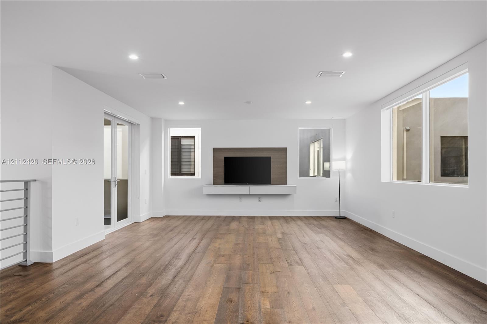 Spacious interior featuring wood-finish flooring, recessed lighting, and a custom built-in wall unit with an integrated media backdrop