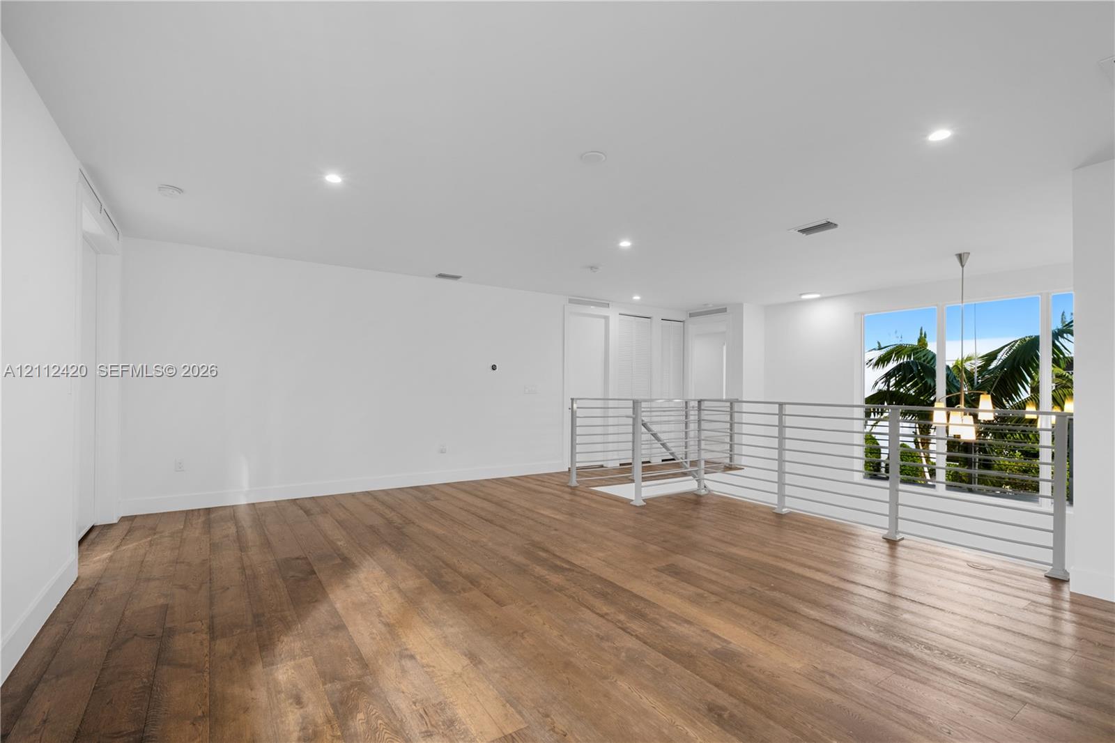 Open-concept area featuring wood-finish flooring, recessed lighting, and a metal horizontal-bar railing