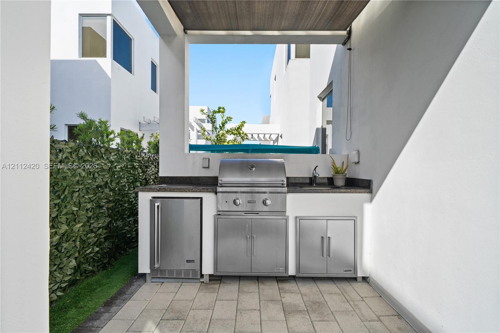Outdoor kitchen featuring a stone-topped counter, stainless steel grill, under-counter refrigeration, built-in cabinetry, and a prep sink, set upon a paved patio