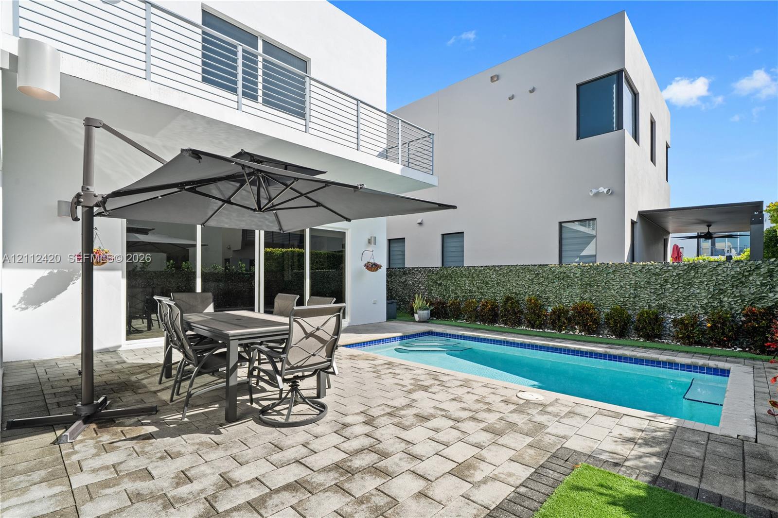 Modern exterior featuring a paved stone patio, in-ground swimming pool, horizontal metal balcony railing, and floor-to-ceiling sliding glass doors