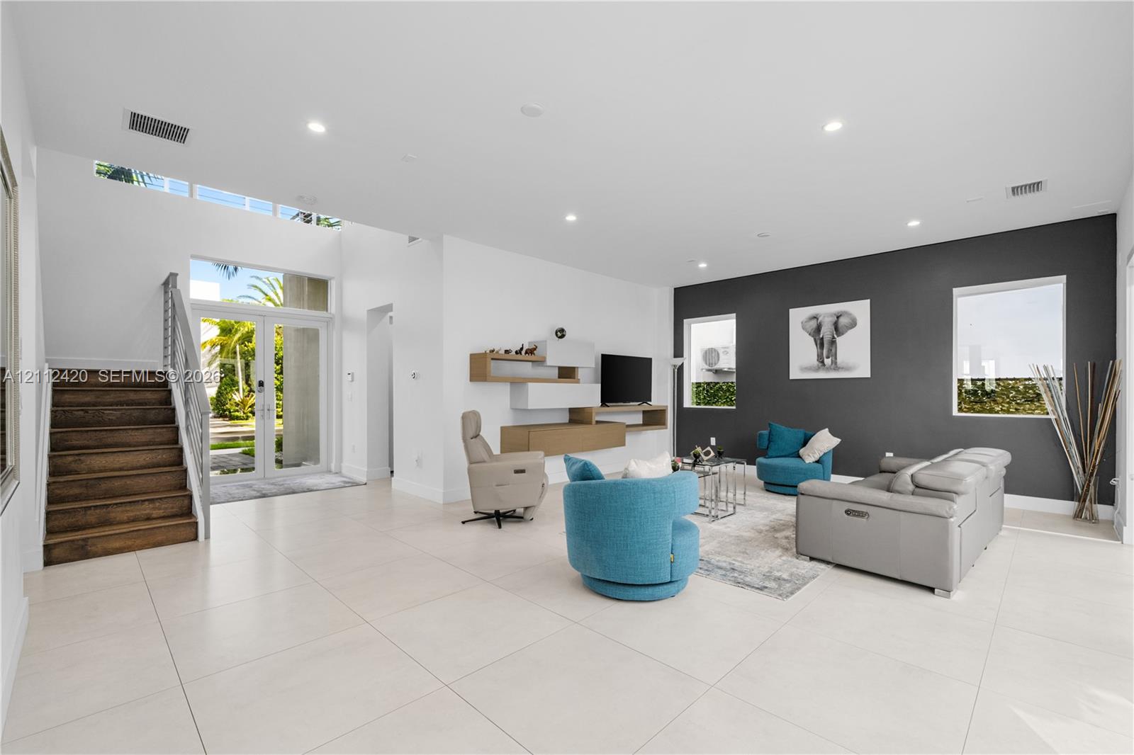 High-ceiling open interior featuring large-format tile flooring, a charcoal accent wall, recessed lighting, and a staircase with wood-finish treads