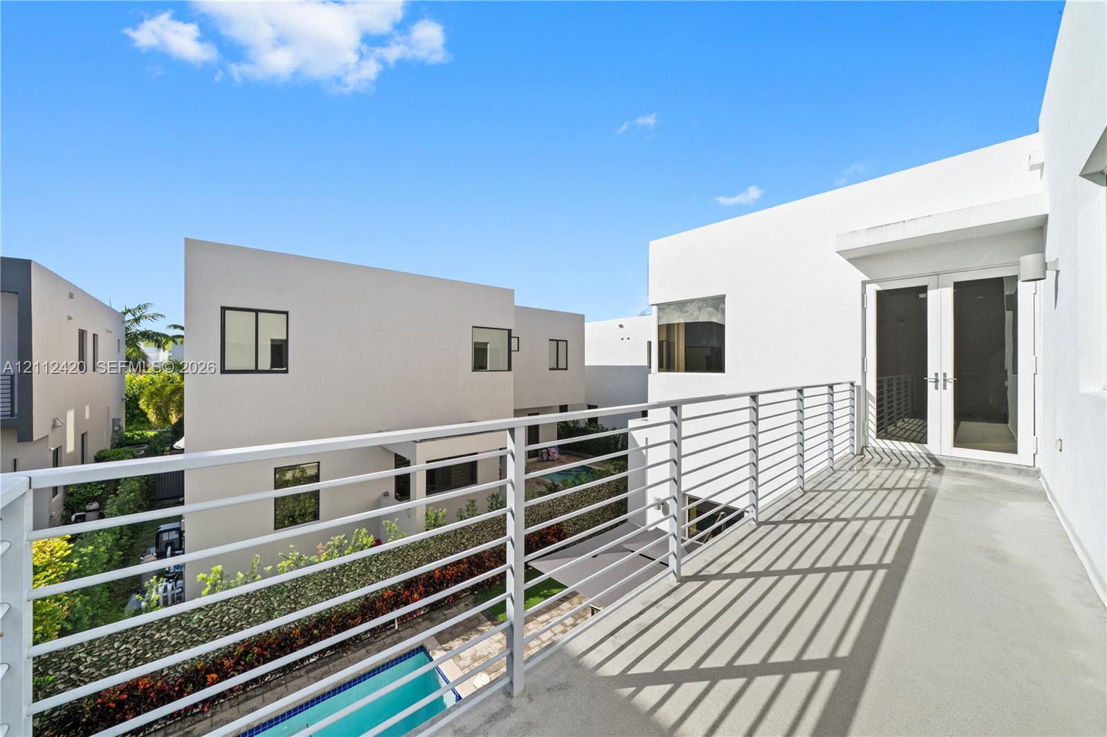 Modern balcony featuring sleek metal railing, smooth concrete flooring, and double-glass entry doors