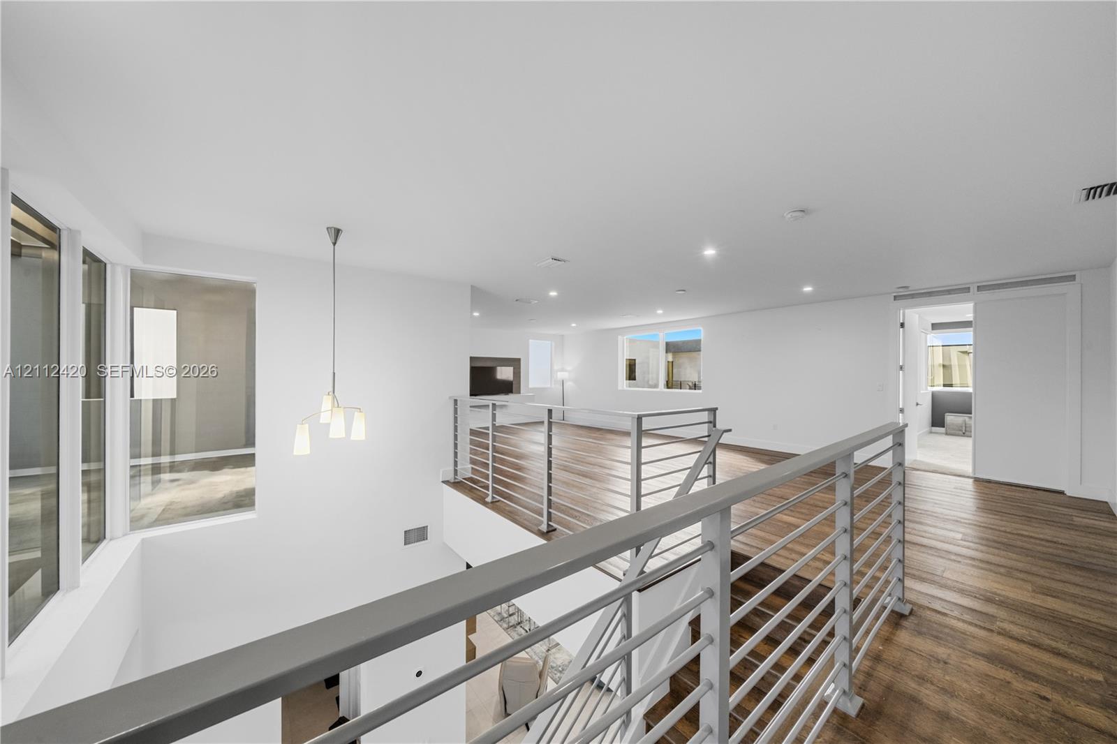 Open-concept interior featuring wood-finish flooring, a multi-light pendant fixture, horizontal metal railing system, and recessed lighting