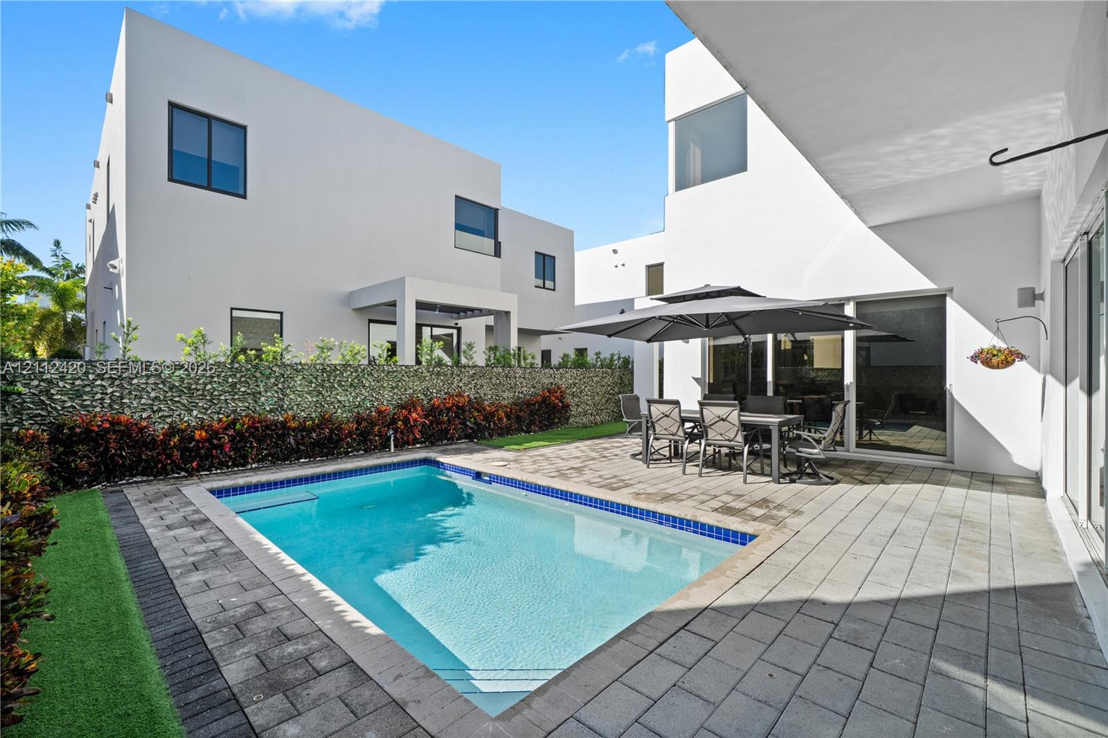 In-ground swimming pool with a tiled perimeter, expansive stone-paver patio, and perimeter wall with integrated greenery