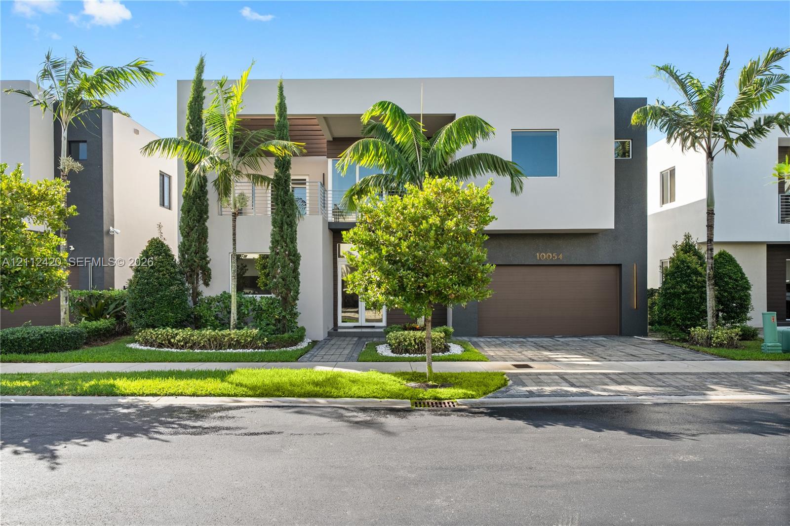 Contemporary two-story exterior featuring a smooth stucco finish, attached two-car garage with solid door, second-level balcony with metal railing, and paver driveway Contemporary two-story exterior featuring a smooth stucco finish, attached two-car garage with solid door, second-level balcony with metal railing, and paver driveway
