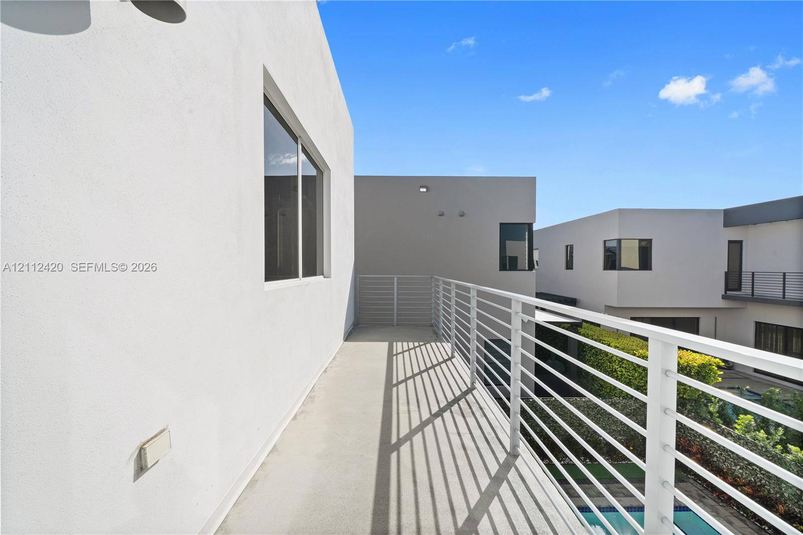Modern balcony featuring white stucco exterior walls, horizontal slat metal railing, and smooth concrete flooring