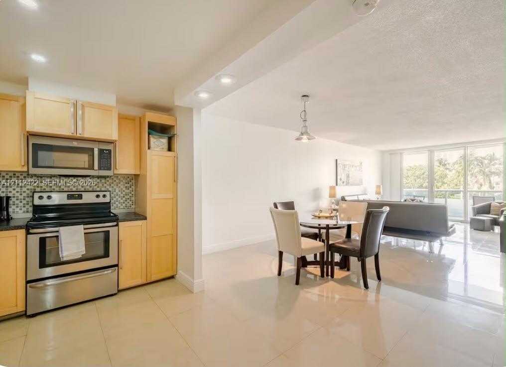 Kitchen featuring light-finish cabinetry, stainless steel appliances, and a decorative tile backsplash, paired with large-format tile flooring and recessed lighting