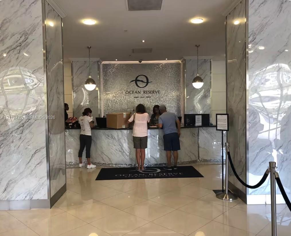 Lobby reception area featuring floor-to-ceiling stone-clad pillars, polished tile flooring, metallic mosaic accent wall, and dual pendant lighting fixtures