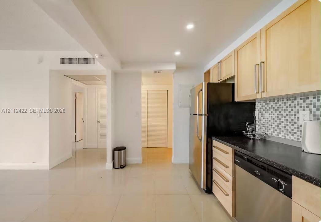 Kitchen featuring light-wood cabinetry, dark stone-finish countertops, stainless steel appliances, and a mosaic tile backsplash