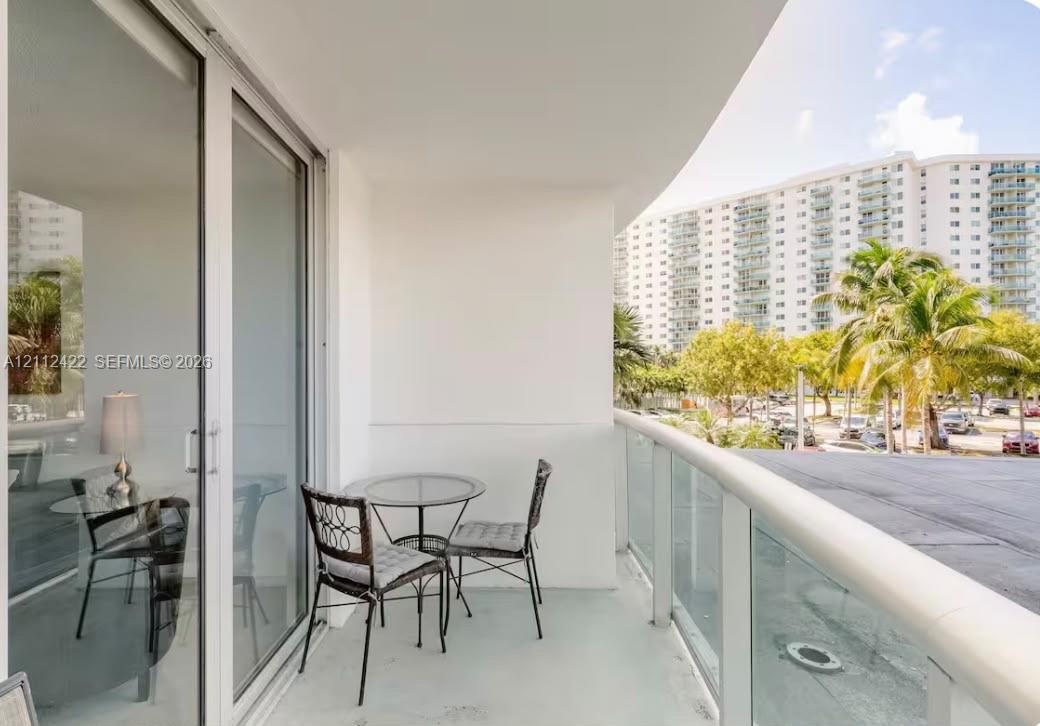 Covered balcony featuring a glass panel railing, painted concrete flooring, and sliding glass door access