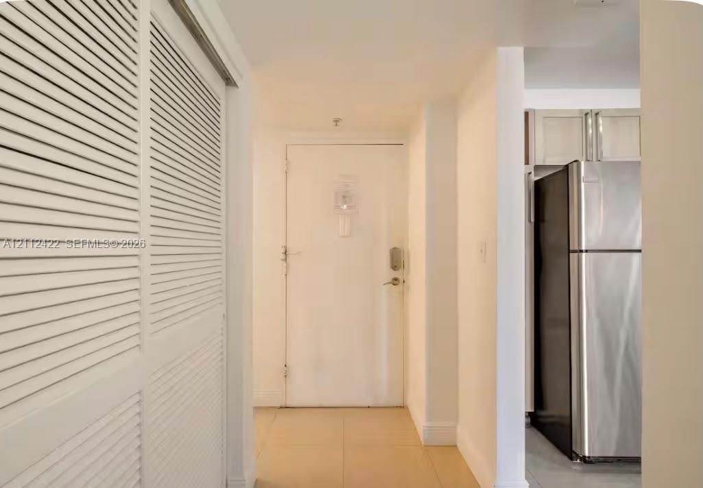 Entryway featuring dual louvered-door closets, neutral tile flooring, and a stainless steel refrigerator