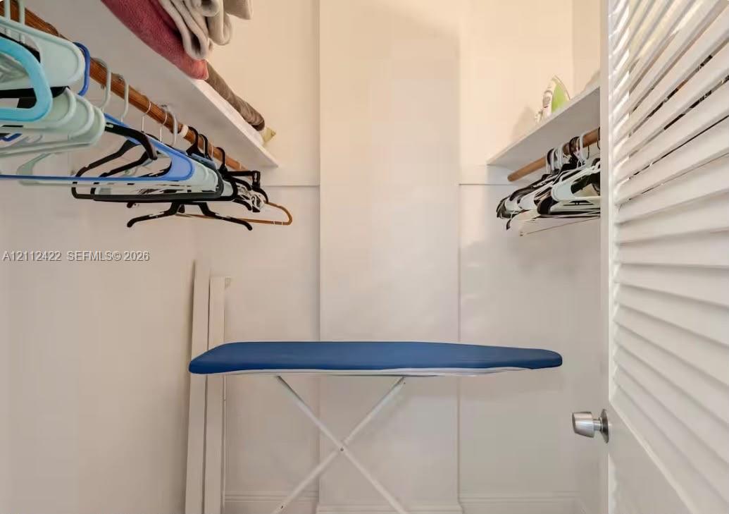 Walk-in storage space featuring built-in shelving, wooden garment rods, and a white louvered door