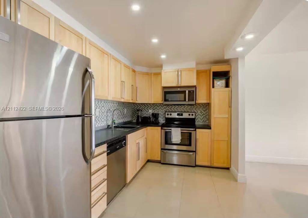 Kitchen featuring light-finish cabinetry, stainless steel appliances, dark countertops, a geometric-patterned tile backsplash, and recessed lighting