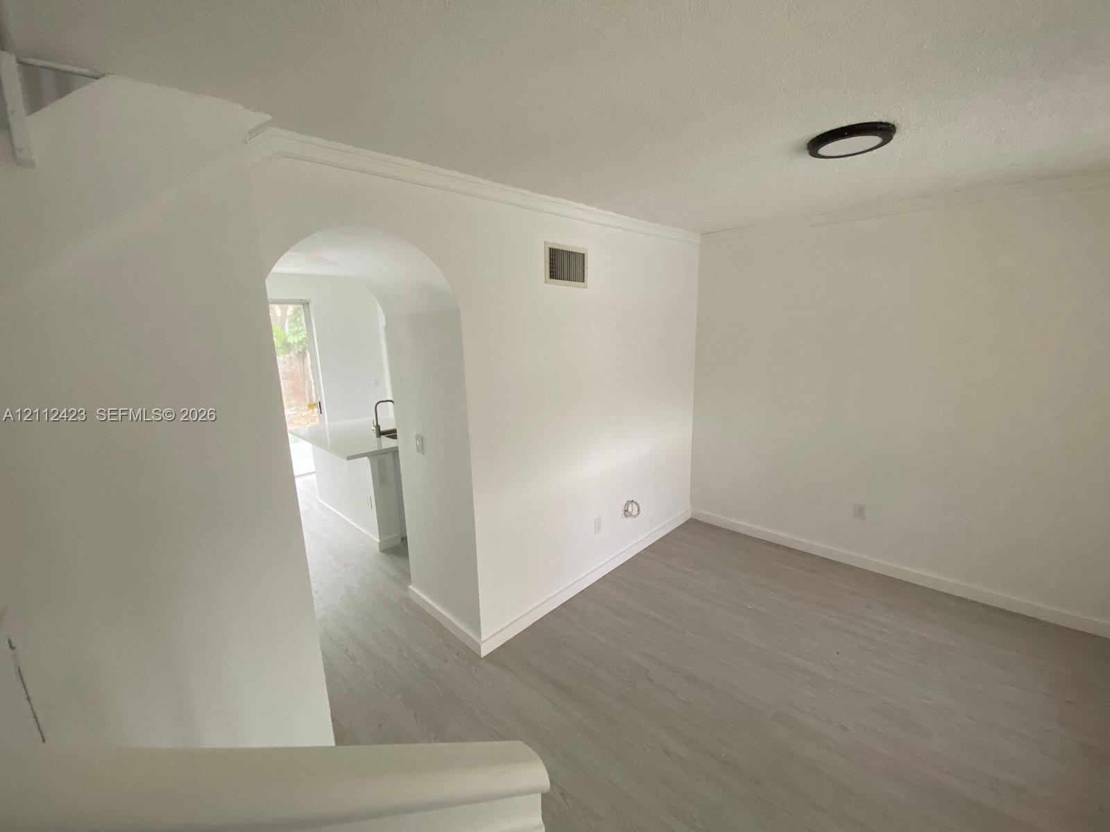 Wood-finish flooring, architectural arched opening, and flush-mount ceiling lighting