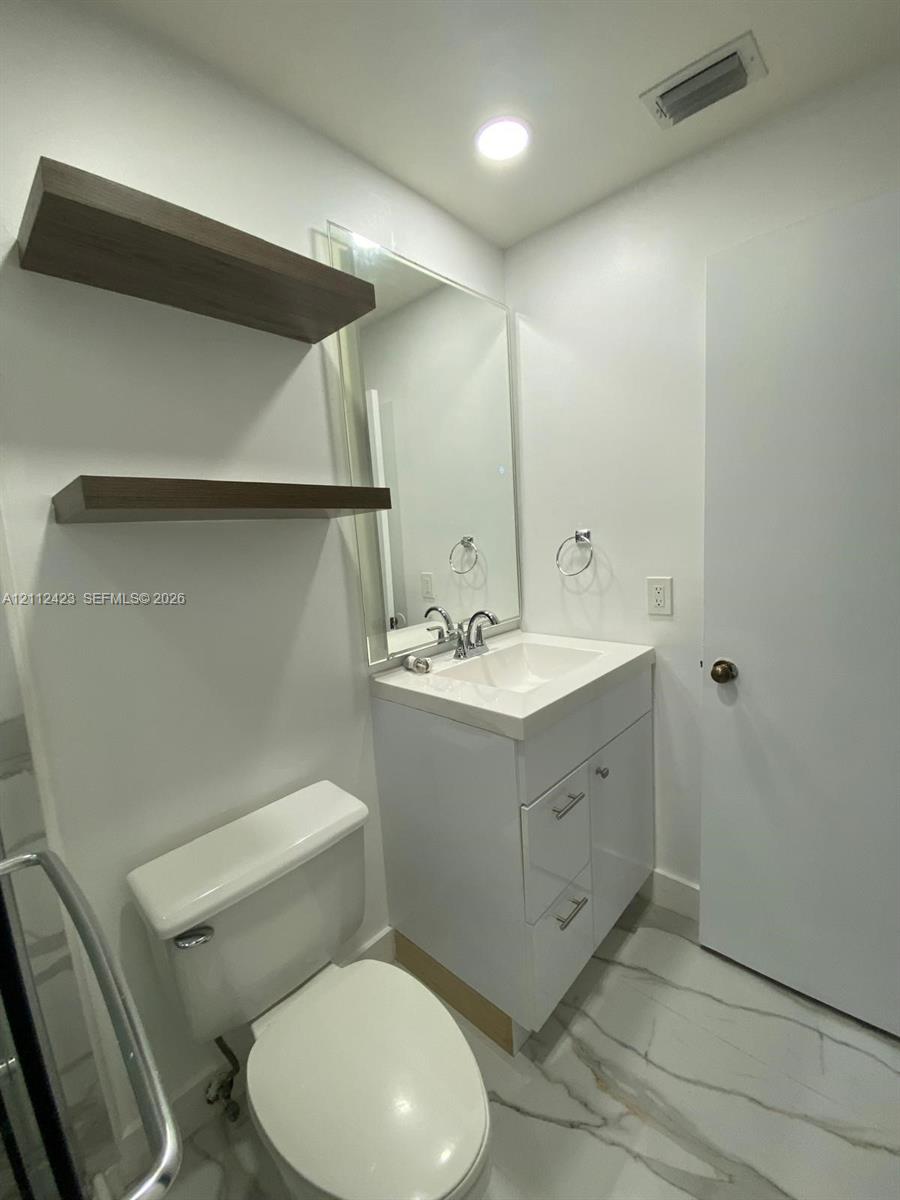 Modern vanity featuring a white cabinet, integrated sink, and chrome faucet, complemented by wall-mounted wood-finish floating shelves, a large wall mirror, and stone-finish tile flooring