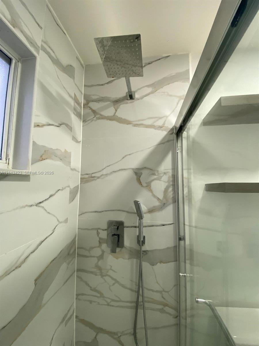 Shower enclosure featuring large-format veined tile surround, overhead rainfall showerhead, wall-mounted handheld sprayer, and built-in shelving