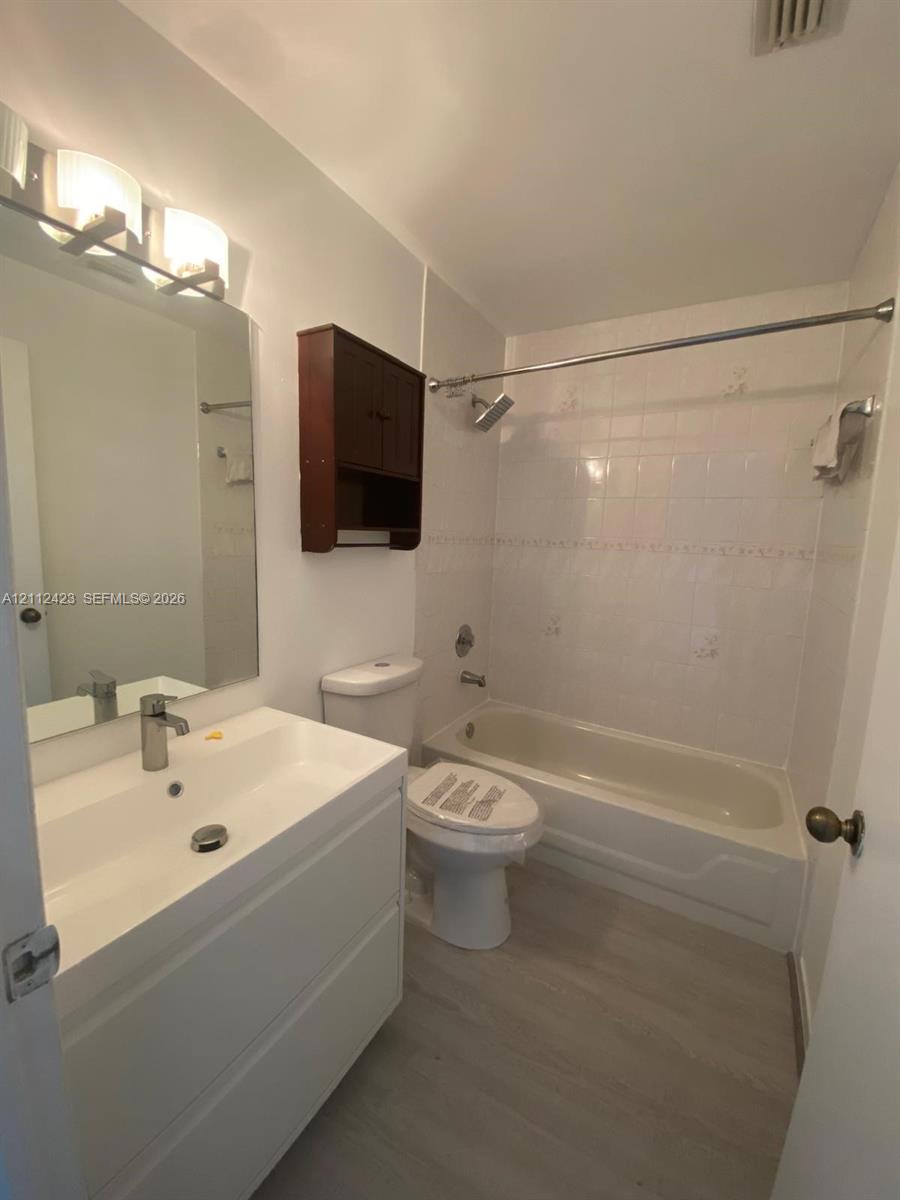 Modern vanity with a rectangular sink, chrome-finish faucet, full-width mirror, wall-mounted storage cabinet, and wood-finish flooring