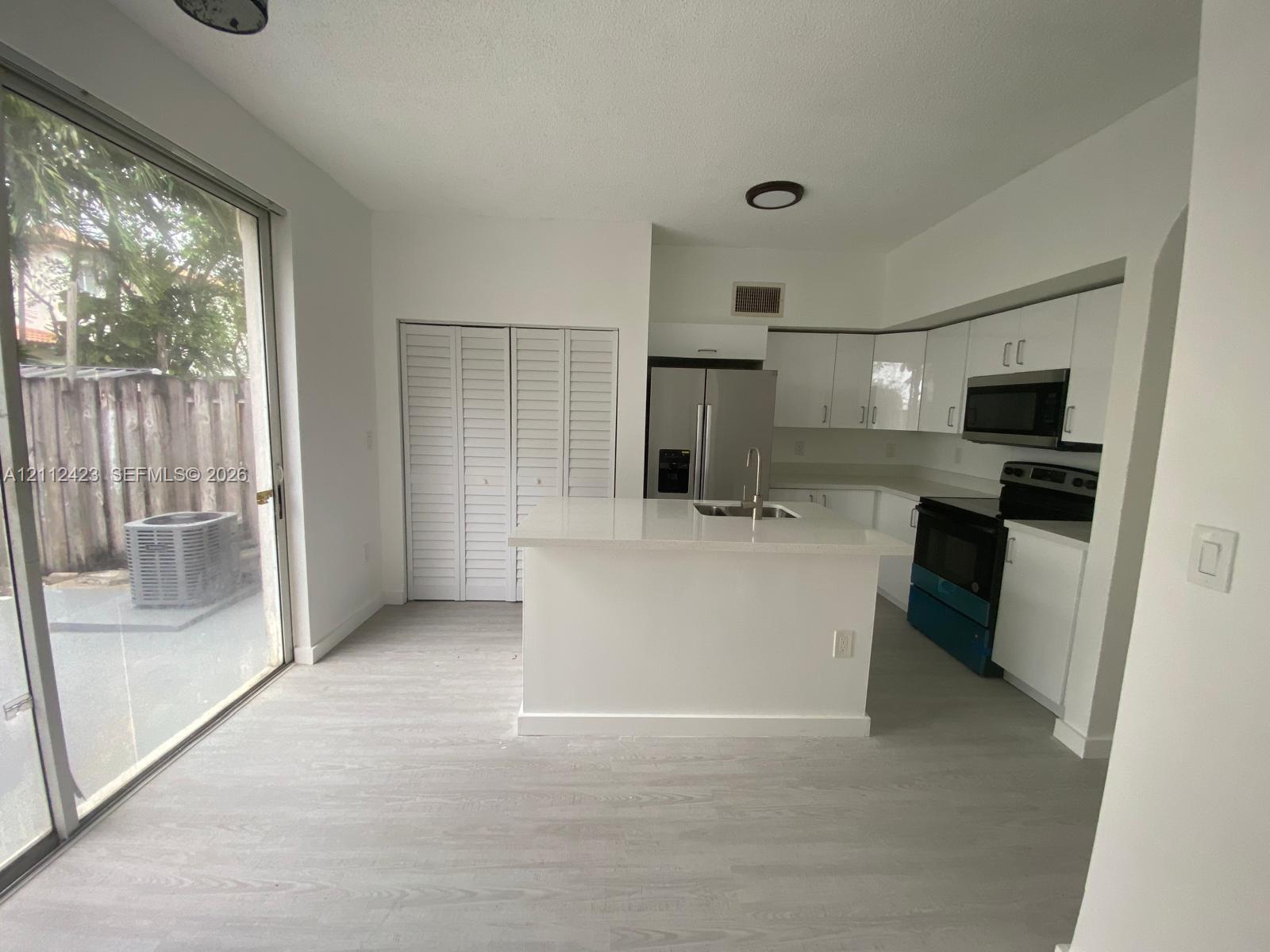 Kitchen featuring white cabinetry, a center island with a stone-finish countertop, stainless steel appliances, sliding glass doors, and wood-finish flooring