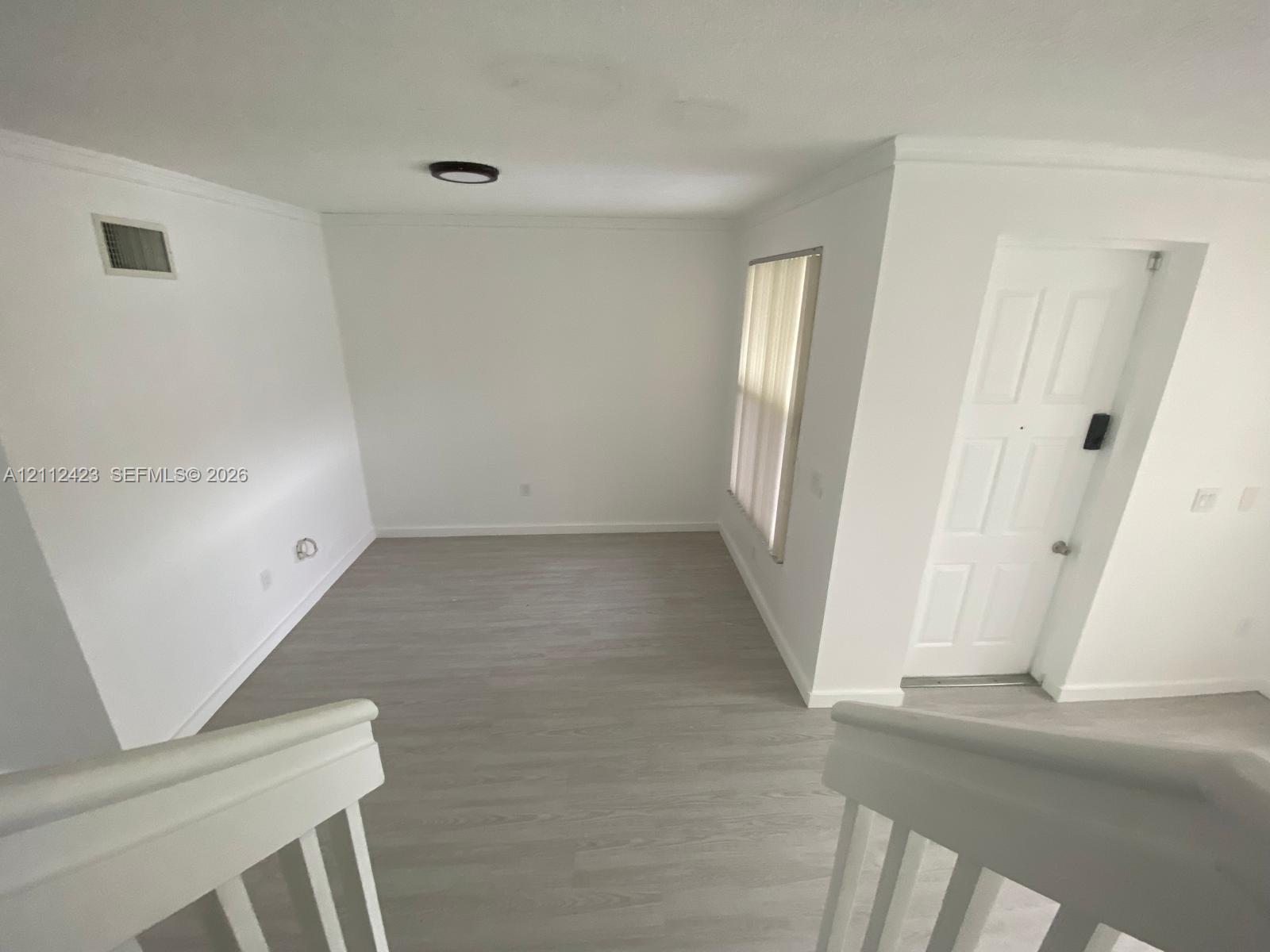 Interior space featuring wood-finish flooring, a six-panel door, crown molding, and a minimalist flush-mount ceiling light fixture