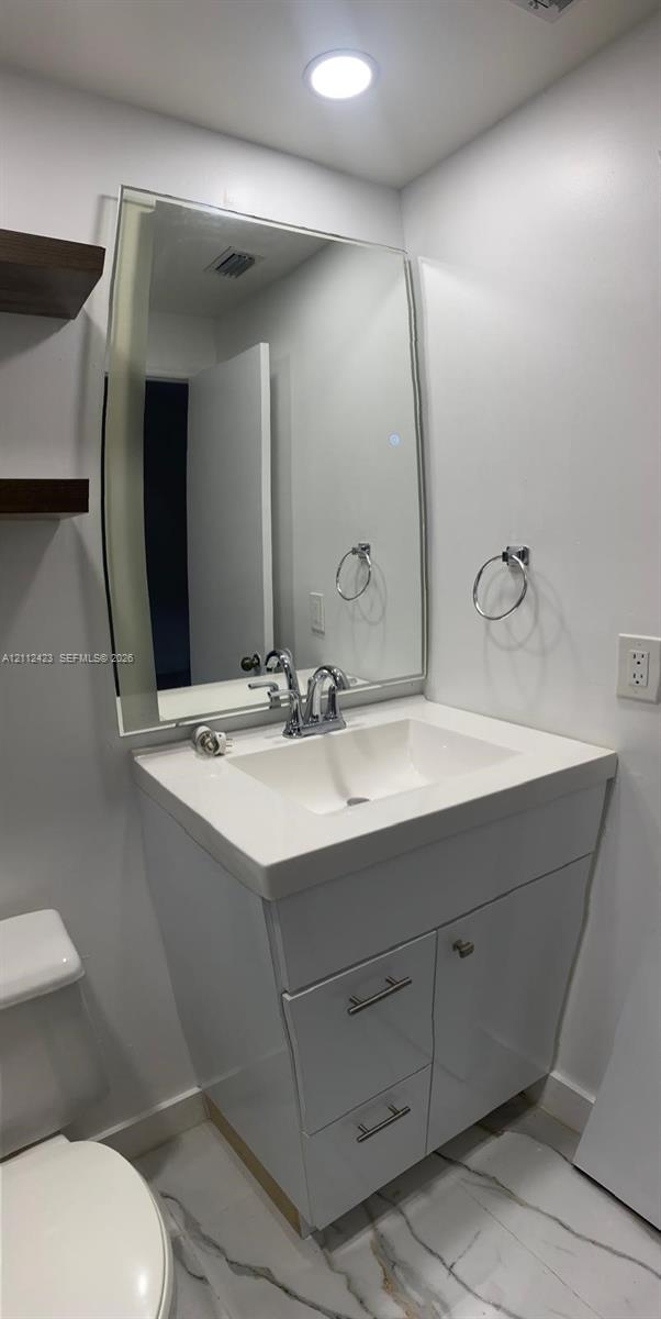 White vanity featuring an integrated rectangular sink, stone-finish countertop, polished chrome faucet, large rectangular mirror, and floating wall-mounted shelving