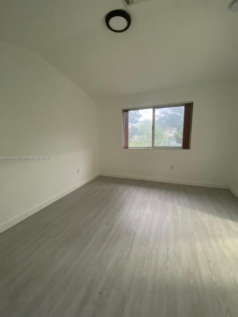 Room interior featuring light-toned wood-finish flooring, neutral walls, a single horizontal window, and a circular flush-mount ceiling light fixture