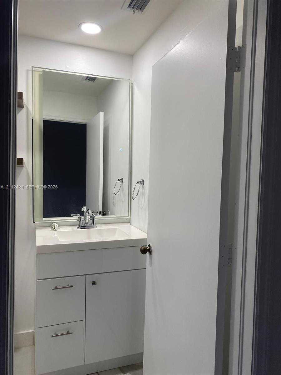 White vanity with a rectangular sink, integrated solid-surface countertop, polished chrome hardware, and a frameless wall-mounted mirror