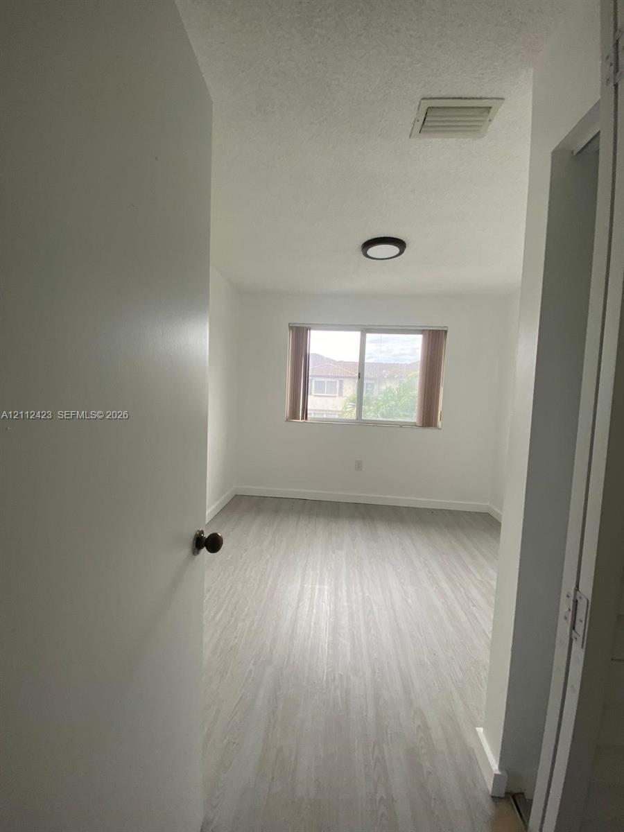 Interior room featuring neutral wall finishes, wood-finish flooring, a flush-mount circular light fixture, and a dual-pane sliding window
