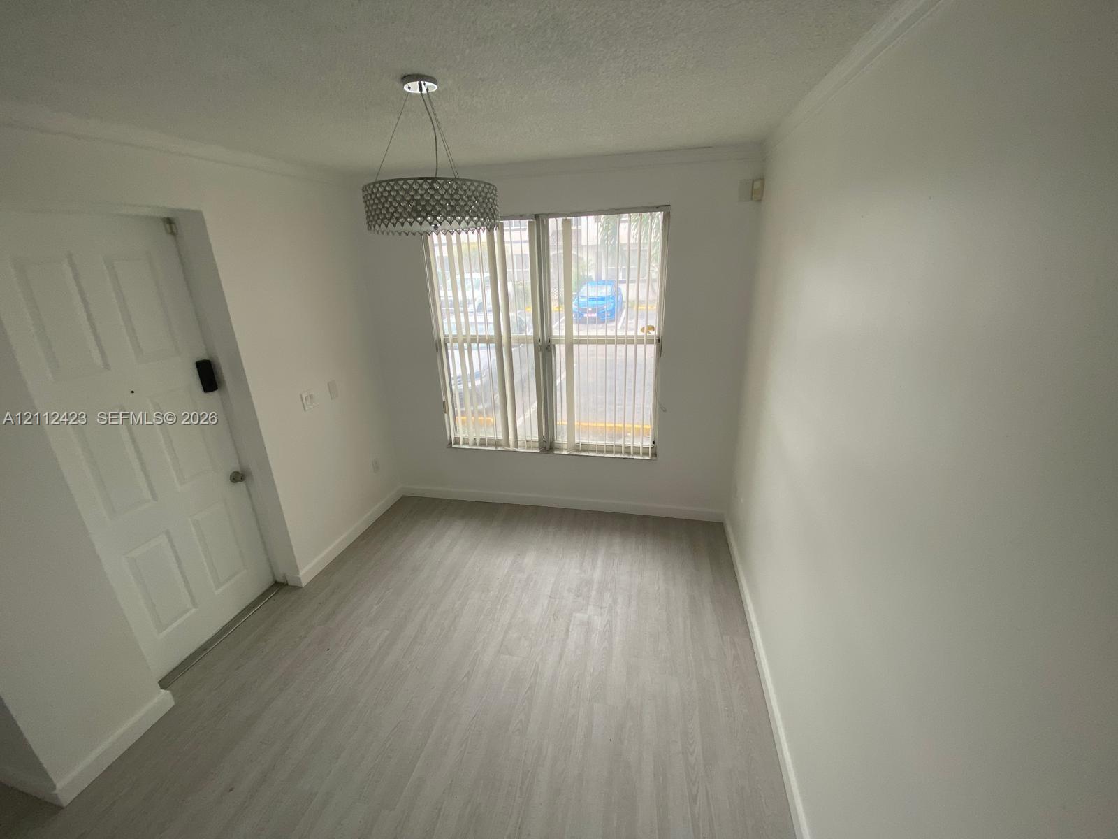 Neutral interior space featuring wood-finish flooring, a drum-style pendant light fixture, vertical window blinds, and a paneled entry door