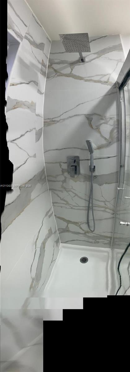 Walk-in shower featuring floor-to-ceiling stone-finish tile, rainfall showerhead, adjustable handheld shower wand, and glass enclosure