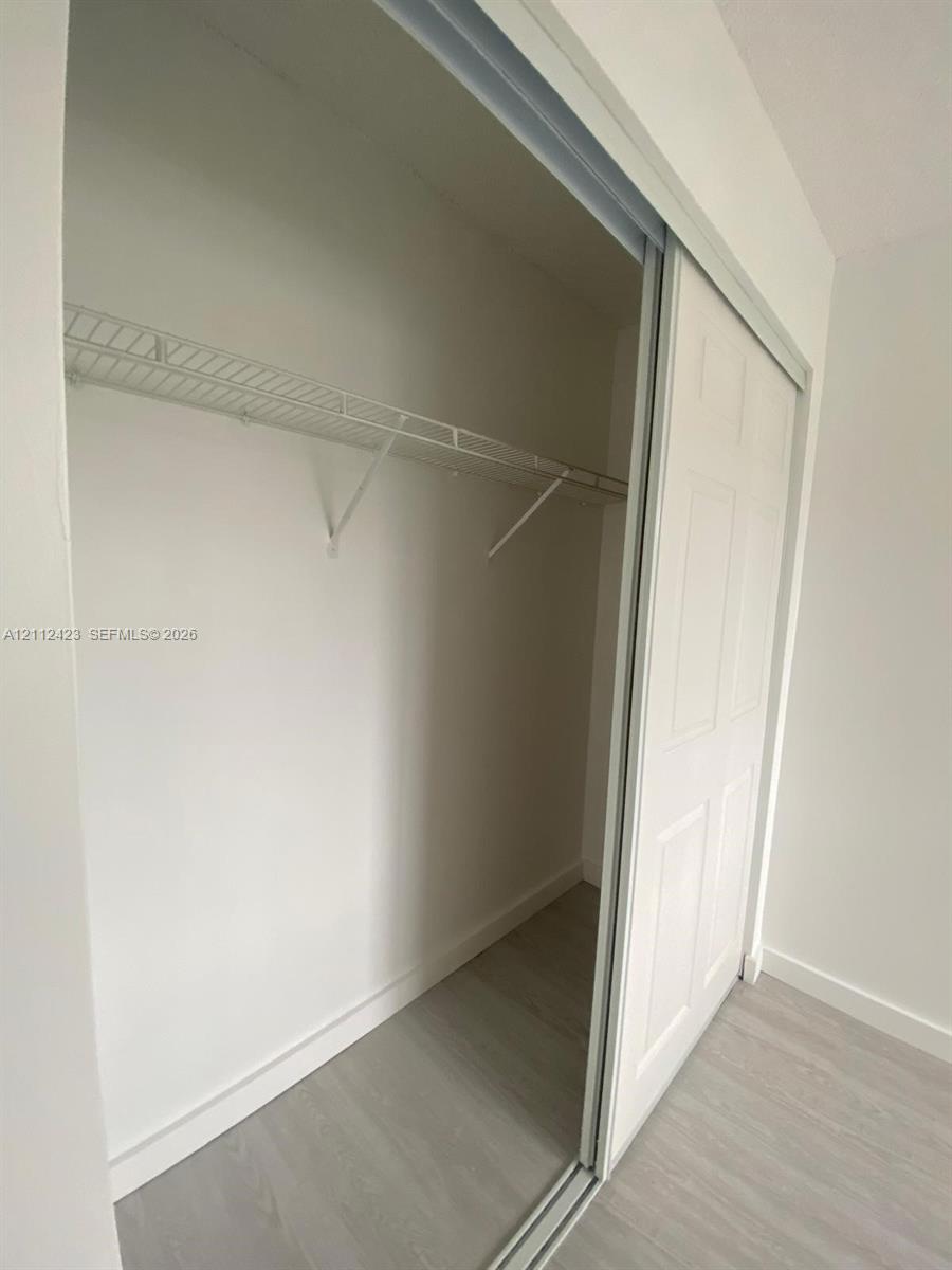 Reach-in closet featuring white multi-panel sliding doors, interior wire shelving, and wood-finish flooring