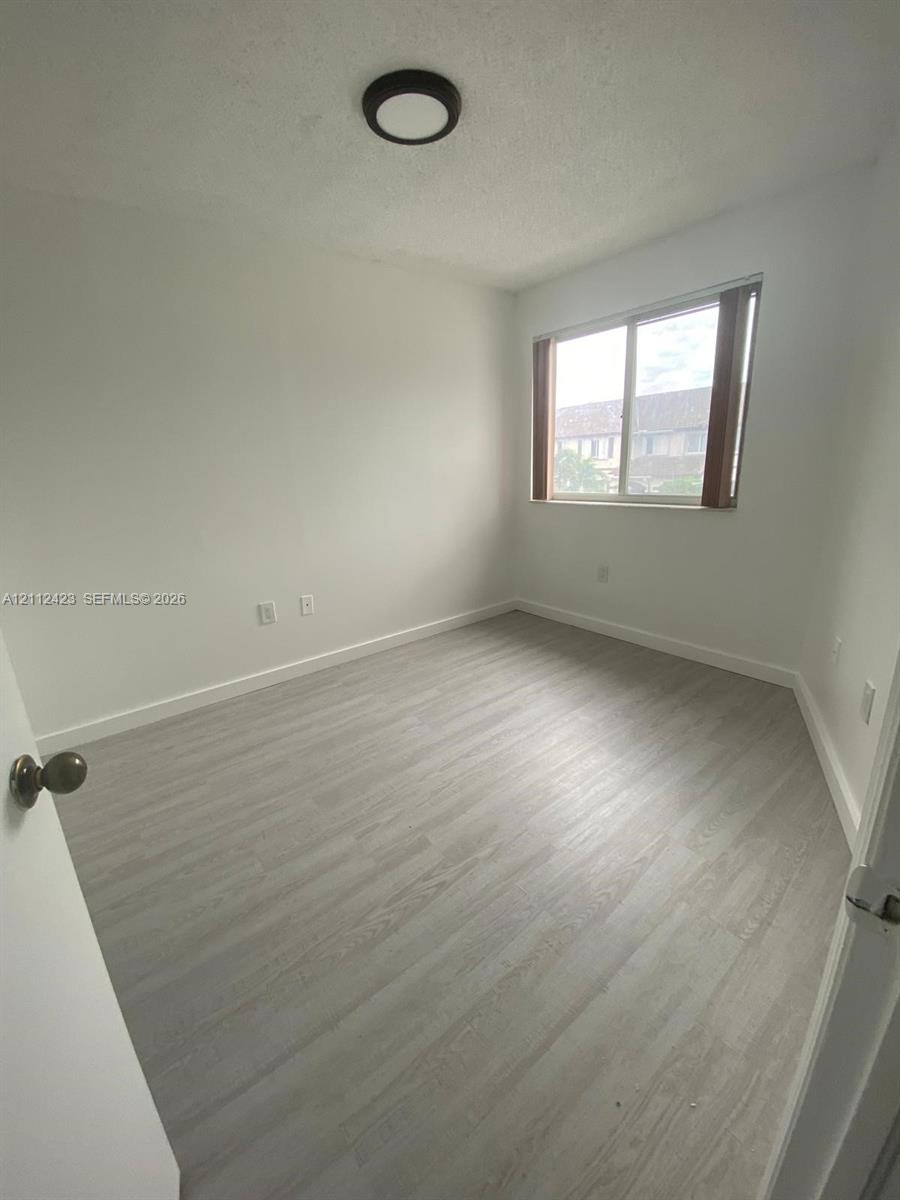 Room featuring light-toned wood-finish flooring, a sliding window with neutral trim, and a low-profile flush-mount ceiling light