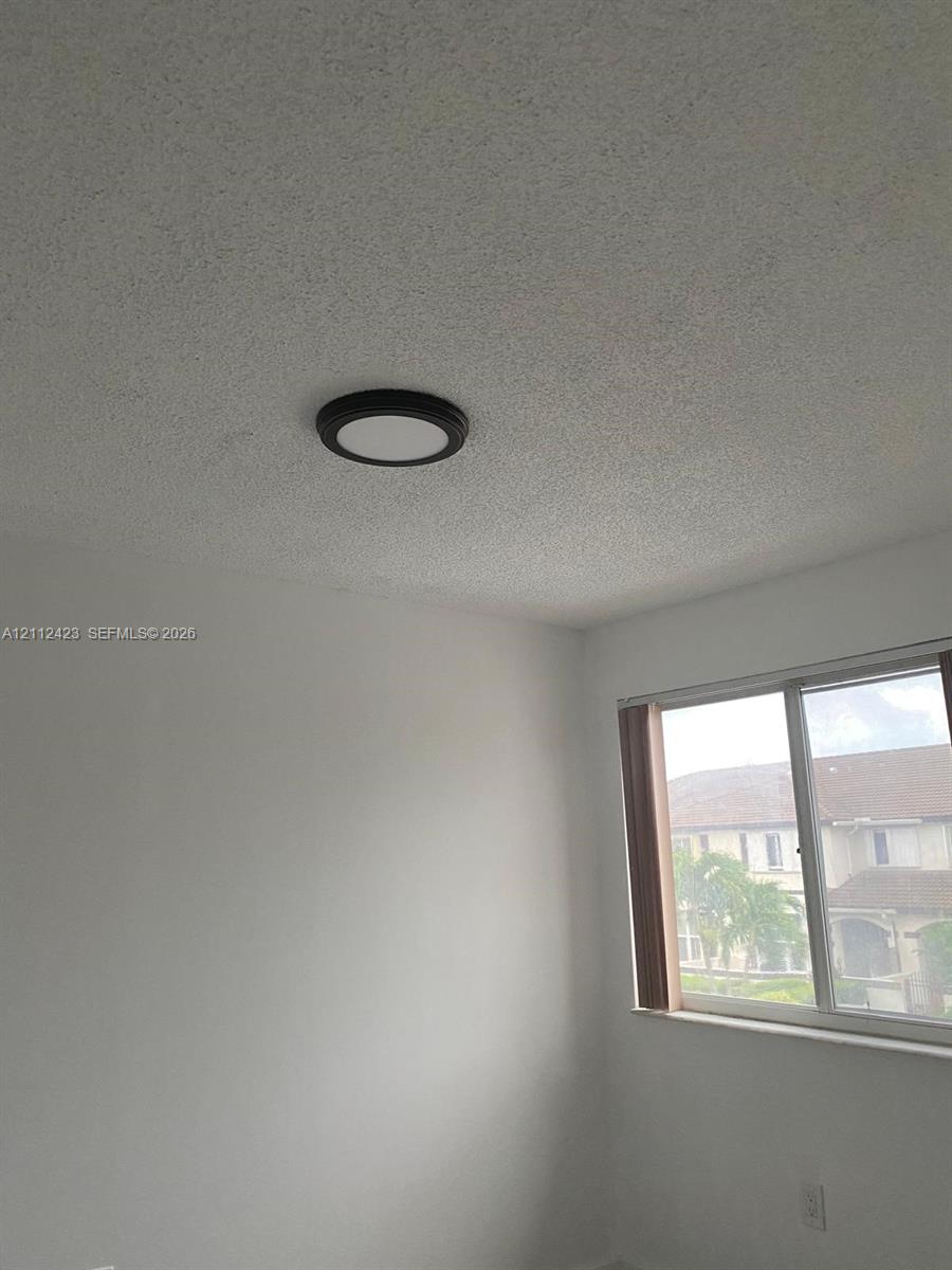 Interior room featuring white-painted walls, a textured ceiling, and a circular flush-mount ceiling light with a dark frame