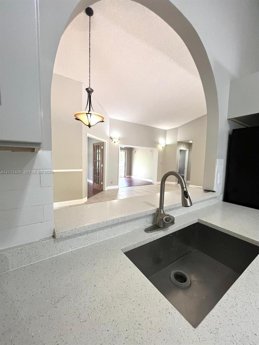 Kitchen featuring stone-finish countertops, undermount sink with arched pull-down faucet, white subway tile backsplash, and a prominent arched pass-through window with an integrated pendant light