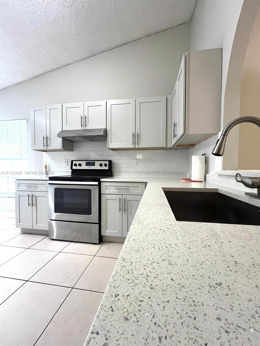 Kitchen featuring light-toned shaker cabinetry, stone-composite countertops, stainless steel appliances, a white tile backsplash, and ceramic floor tiling