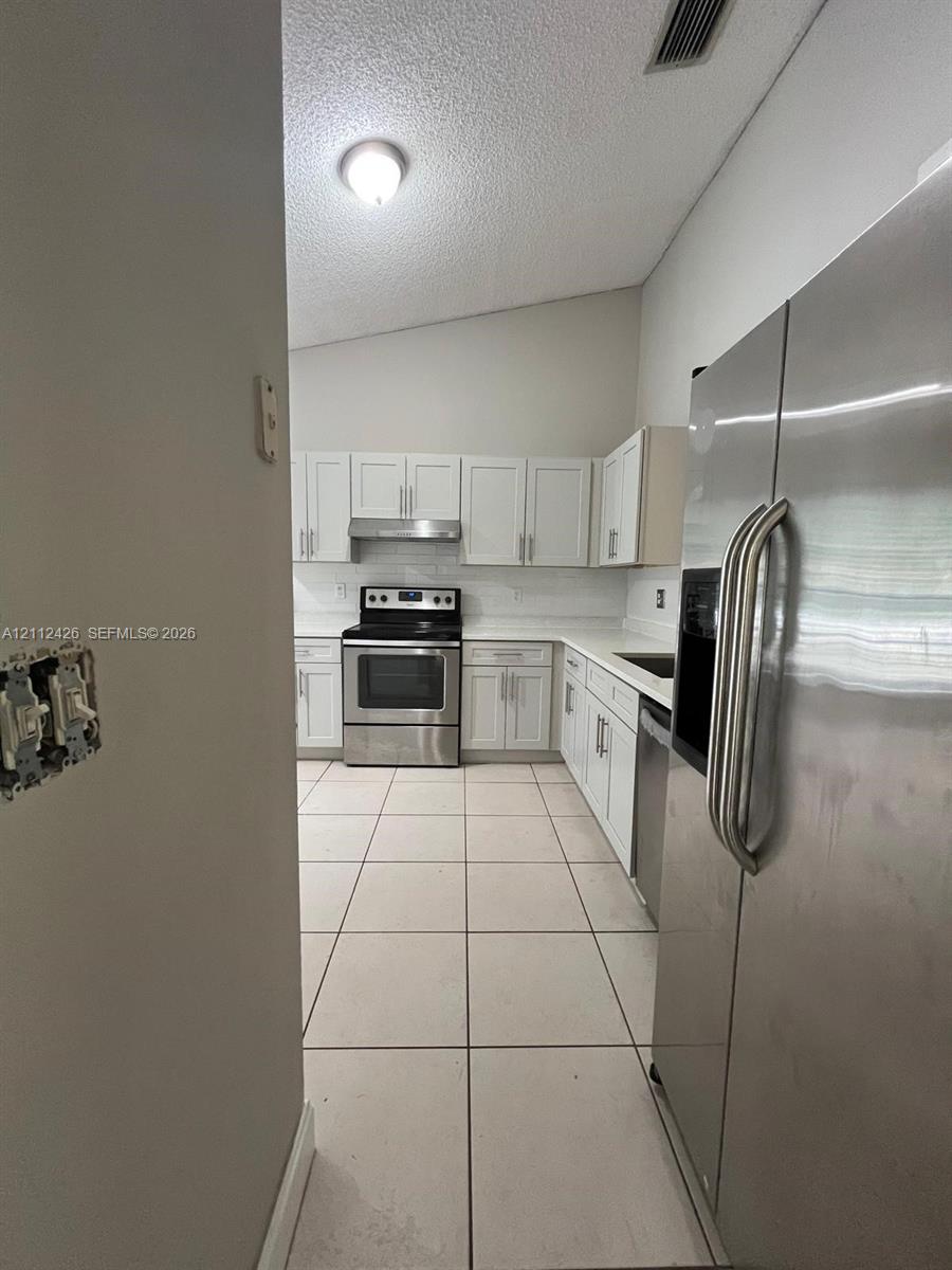 Kitchen featuring white cabinetry, solid-surface countertops, stainless steel appliances, and tile flooring under a vaulted ceiling