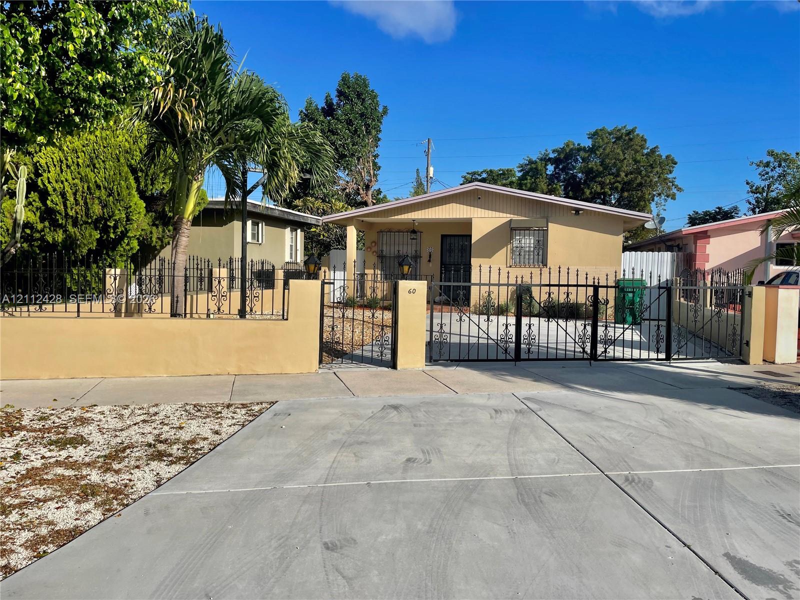 Single-story residence featuring a concrete driveway, gated perimeter wall, ornate metal fencing, and a covered entryway Single-story residence featuring a concrete driveway, gated perimeter wall, ornate metal fencing, and a covered entryway
