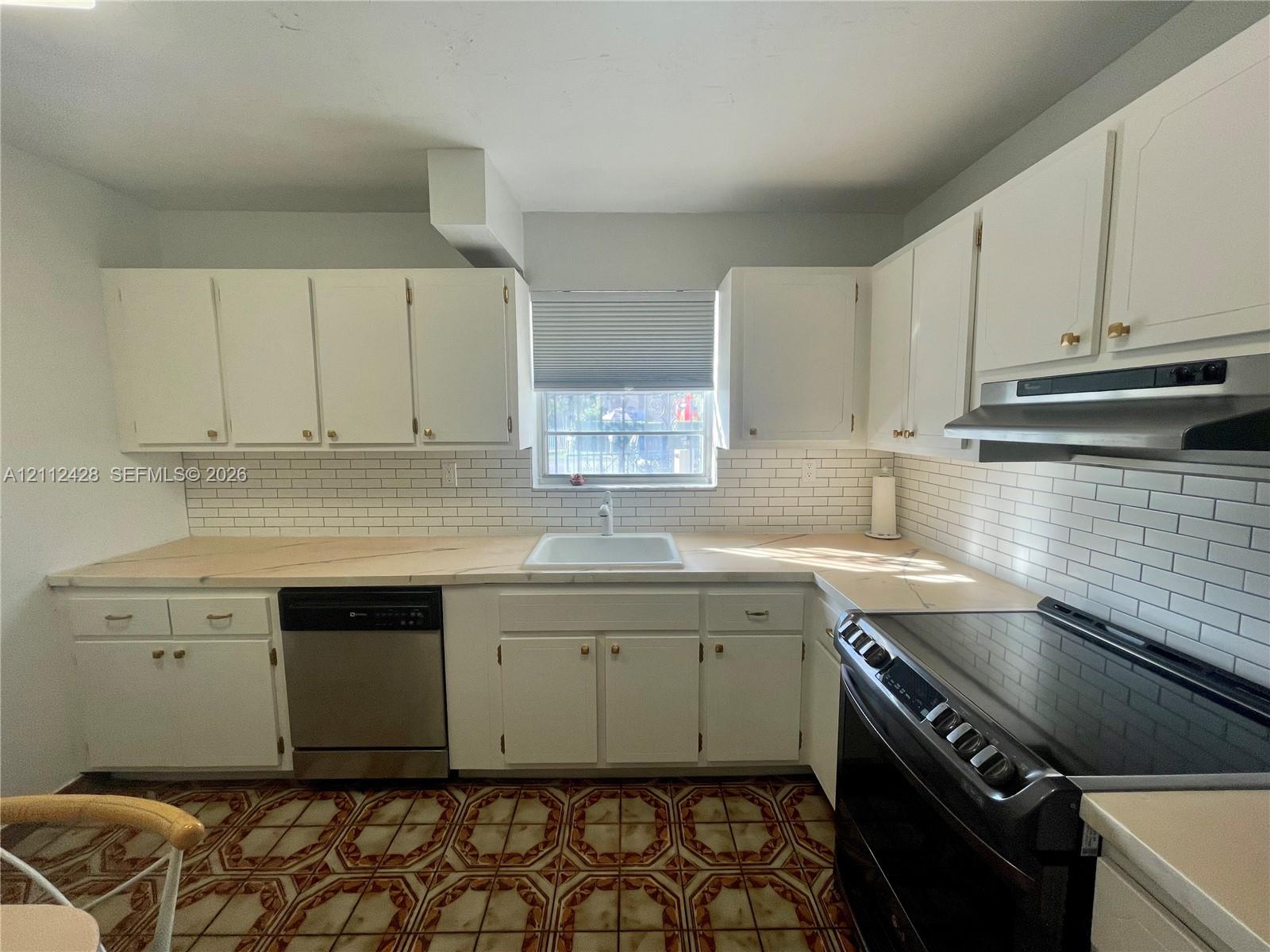 Kitchen featuring white cabinetry, subway tile backsplash, stainless steel dishwasher, integrated range hood, and light-toned countertops with an undermount sink Kitchen featuring white cabinetry, subway tile backsplash, stainless steel dishwasher, integrated range hood, and light-toned countertops with an undermount sink
