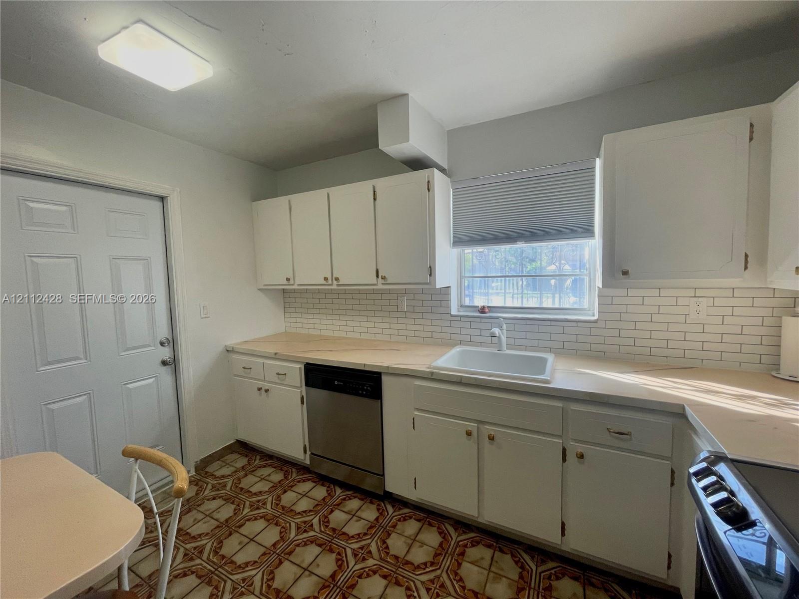 Kitchen featuring white cabinetry, subway tile backsplash, integrated stainless steel dishwasher, and a single-basin sink with a gooseneck faucet Kitchen featuring white cabinetry, subway tile backsplash, integrated stainless steel dishwasher, and a single-basin sink with a gooseneck faucet