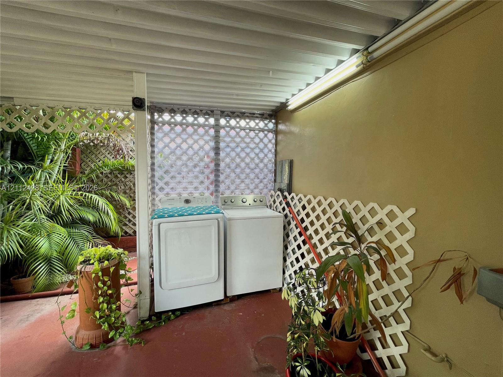 Covered outdoor laundry area featuring white lattice wall panels, corrugated metal ceiling, and concrete flooring