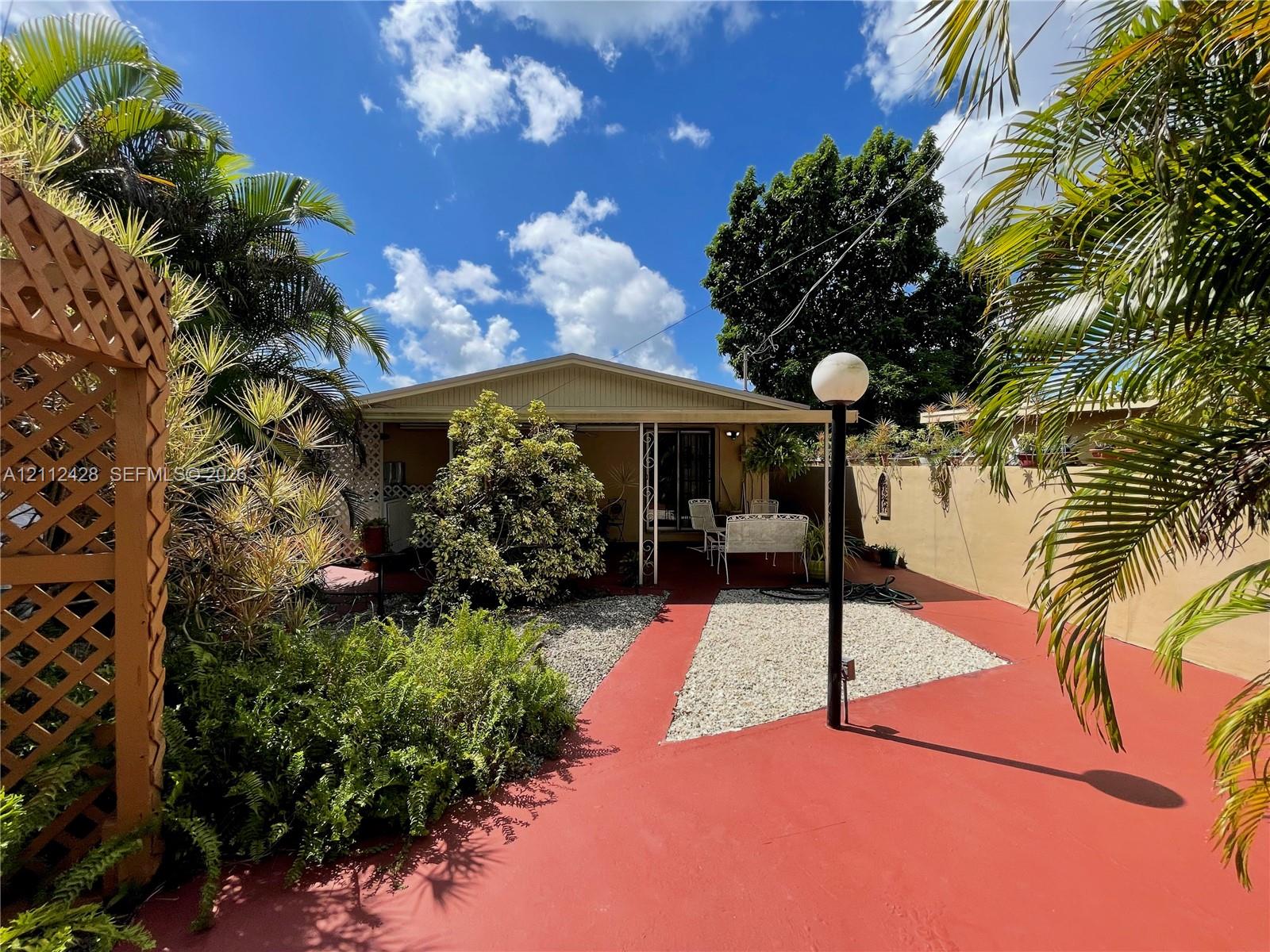 Enclosed courtyard featuring painted concrete flooring, stone-accented ground cover, decorative wood lattice screening, and mature tropical landscaping Enclosed courtyard featuring painted concrete flooring, stone-accented ground cover, decorative wood lattice screening, and mature tropical landscaping