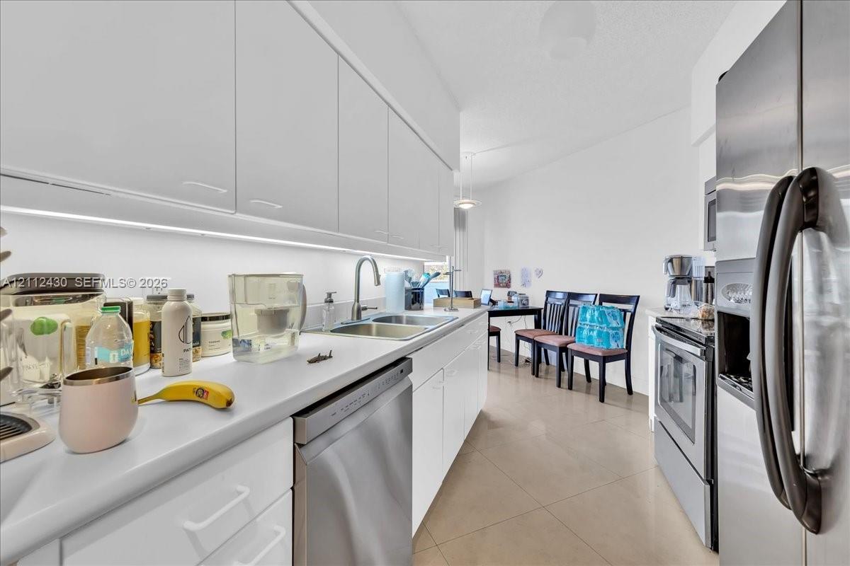 Kitchen featuring flat-panel white cabinetry, solid-surface countertops, stainless steel appliances, under-cabinet lighting, and large-format tile flooring