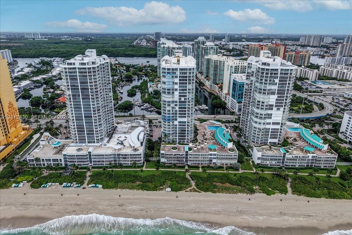 High-rise residential complex featuring beachfront access, podium-level swimming pools, tiered structural design, and glass-paneled balconies