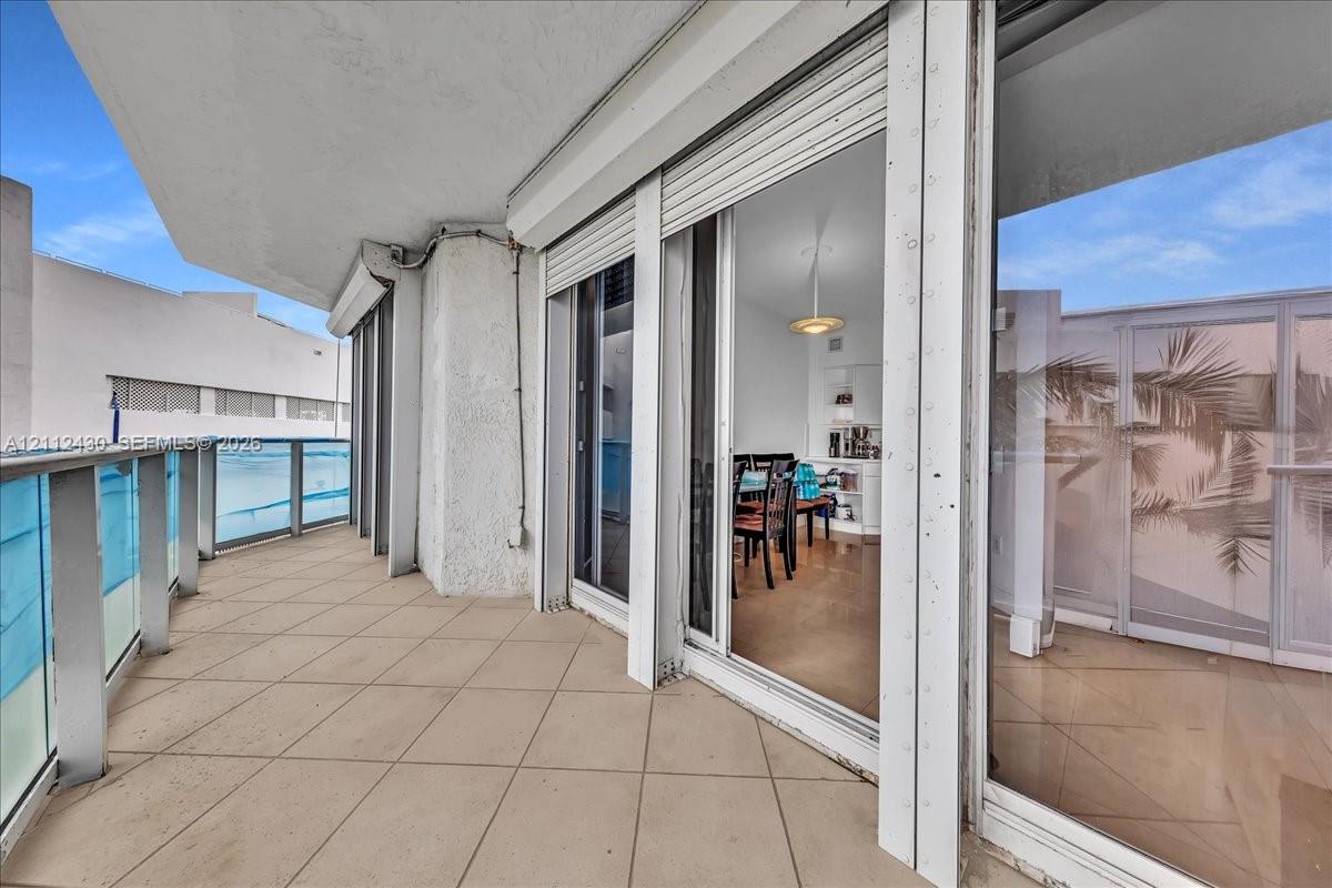 Covered balcony featuring tile flooring, metal and glass railings, and expansive floor-to-ceiling sliding glass doors with integrated shutters